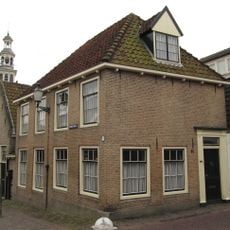 Hoekpand onder schilddak. Oude kozijnen en deuromlijsting door pilasters. Gesneden kalf