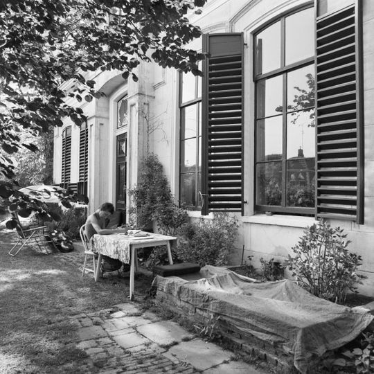 Gebouw op T-vormige plattegrond onder schilddaken met op het dwarshuis hoekschoorstenen met borden