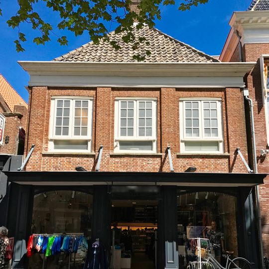 Pand met vernieuwde gevel onder dak met voorschild met topschoorsteen waarop bord