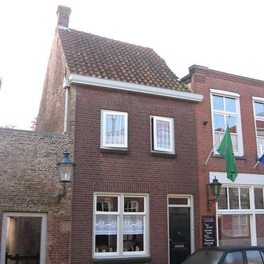 Achter een moderne gevel een huis met dwars zadeldak tussen zijtopgevels