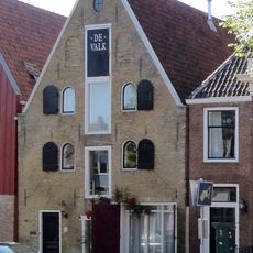 Pakhuis onder zadeldak tegen smalle topgevel met beitelingen en drie rechthoekige hijsluiken