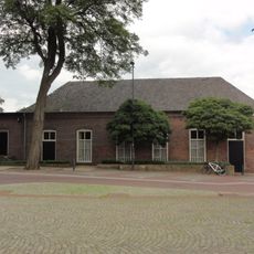 Voormalig schoolgebouw. Rechthoekig pand met getoogde vensters en langgerekt pannen schilddak. Geprofileerde, bakstenen waterlijst onder de dakvoet. Aan de westzijde later verlengd