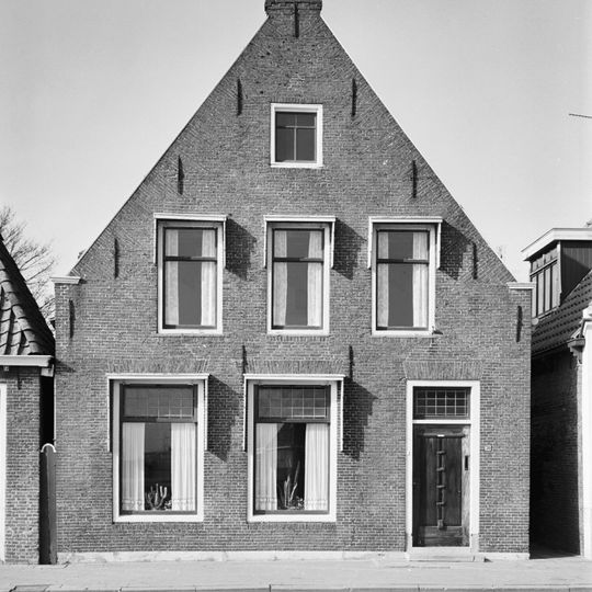 Woonhuis onder zadeldak tegen forse topgevel met beitelingen langs de zijden