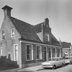 Groot dorpshuis met ingang met Vlaamse top onder zadeldak tussen topgevels waarop hoekschoorstenen met borden (vormt een geheel met nr. 34)