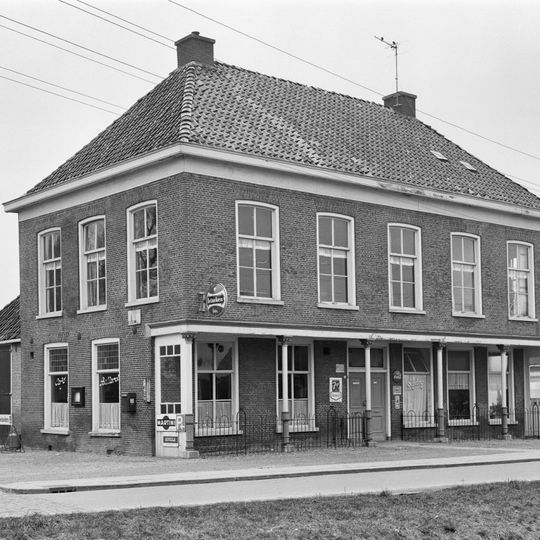 Vijf traveeën breed pand met verdieping die aan voorzijde rust op gietijzeren kolommen, zodat een veranda wordt gevormd