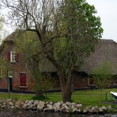 Rustiek gelegen boerderij onder rieten wolfdak. Op het erf een oude roedenberg