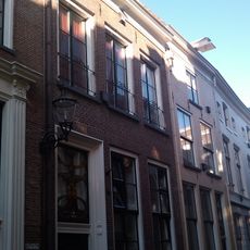 Onderkelderd huis met lijstgevel. Dakkapel. Strekken. Verdieping met vensterhekken. Voordeur met bovenlicht