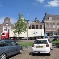 Eenvoudig pand met verdieping met eenvoudige geprofileerde gootlijst met bakgoot op blokjesonder zadeldak met topschoorsteen met bord