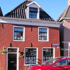 Pand met verdieping met negenruitsvensters onder zadeldak met voorschild met dakkapel en topschoorsteen met bord