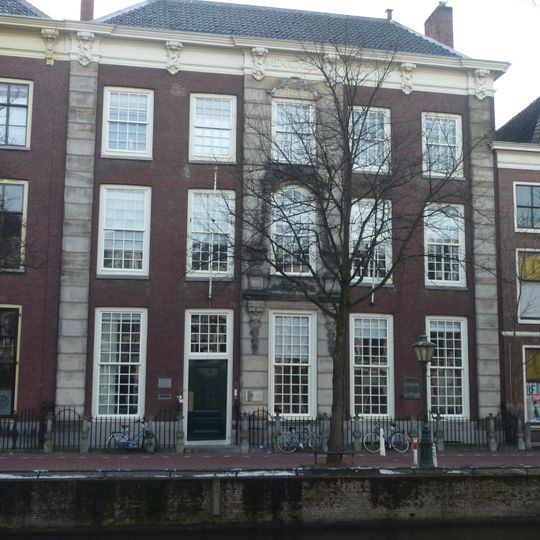 Pand met brede statige bakstenen gevel. Rechte kroonlijst met rocococonsoles, zandstenen geblokte middenpartij met gebeeldhouwde versiering. Gesmeed stoephek en fraaie palen