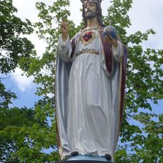 Rzeźba Jezusa stojąca na kamiennym cokole w miejscu powalonego przykościelnego drzewa.