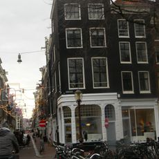 Hoekhuis met voorgevel onder rechte lijst met consoles en gesneden verhoging en boven de gevel van het aangebouwde achterhuis een lijst met consoles