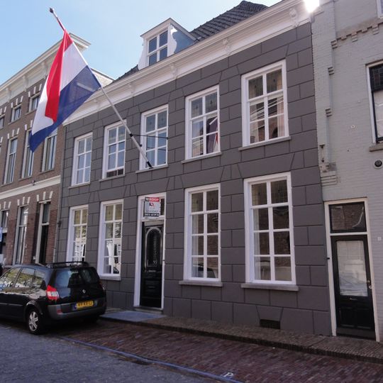 Huis met grijze gebosseerd gepleisterde lijstgevel, kroonlijst op consoles, dwars schilddak, dakkapel en schuiframen, deur