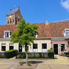 Panden onder lang zadeldak tussen topgevels met aan de westzijde een poortdoorgang naar het kerkhof