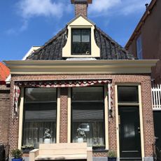 Laag pandje onder schilddak met twee hoekschoorstenen en dakkapel in voorste schild