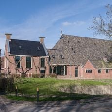 Kop-hals-rompboerderij met onderkelderd voorhuis met zesruitsvensters tussen topgevels waarboven schoorstenen met borden