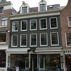 Etagewoningencomplex met gezamenlijke gevel onder rechte lijst en dwars dak waarin twee dakkapellen met snijwerk