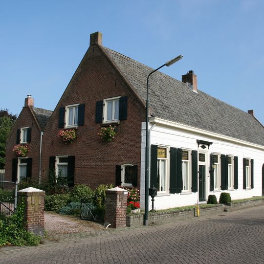 Boerderij van het langgeveltype. Woonhuis en stal onder een pannen zadeldak tussen puntgevels. Lagere aanbouw onder zadeldak tegen de achtergevel.