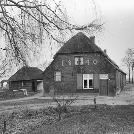 Boerderij van het Kempische langgeveltype, met ingang in de kopgevel, rieten dak met voet van pannen. Met houten schuur onder rieten dak