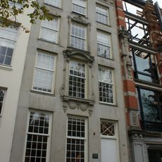 Pand met zandstenen gevel onder rechte triglyfenlijst en attiek, met gebeeldhouwde vensteromlijsting in de as, gebeeldhouwde stoep en deur en kelderpui