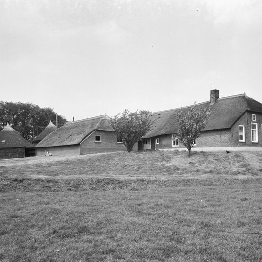 Op terp gelegen boerderij van het Kamper type met rieten zadeldak met wolfschilden, stal onder afgewolfd rieten zadeldak, veelhoekige rieten schuur en hooiberg met rieten kap