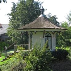 Ahthoekige houten theekoepel in de tuin van dit pand, Lod. XVI met bewerkte daklijst en als bekroning een siervaas op het dak