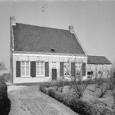 Dorpswoning onder dwars, met pannen belegd zadeldak tussen zijtopgevels. In de gepleisterde voorgevel Empire schuiframen (zesdelig) en jaarankers